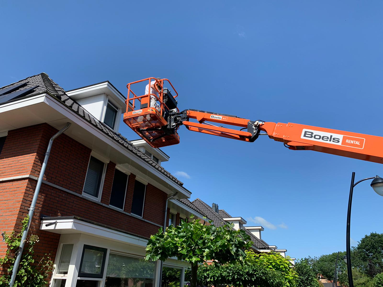 Schilder in een hoogwerker bij een dakkapel en dakrand