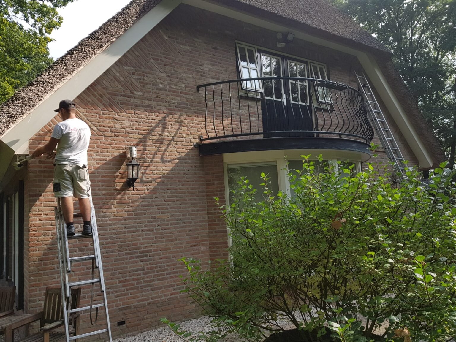 Schilder van MG Schilders op een ladder tijdens buitenschilderwerk aan een woning in Harderwijk